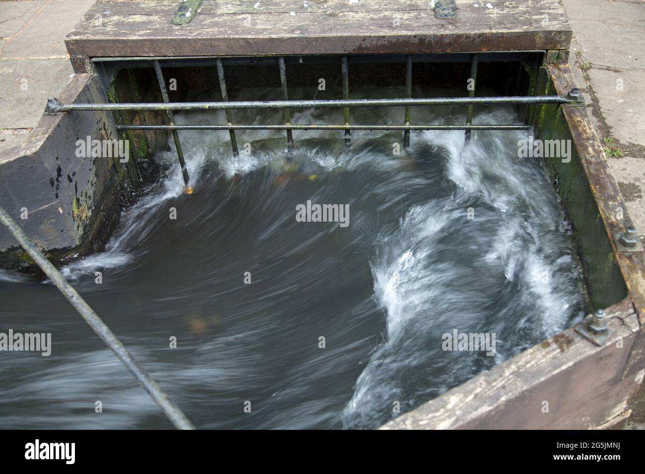 Water rushing down a wooden watercourse towards an exit, possibly a drain or culvert, taken with a slow exposure to show the movement of water Stock Photo