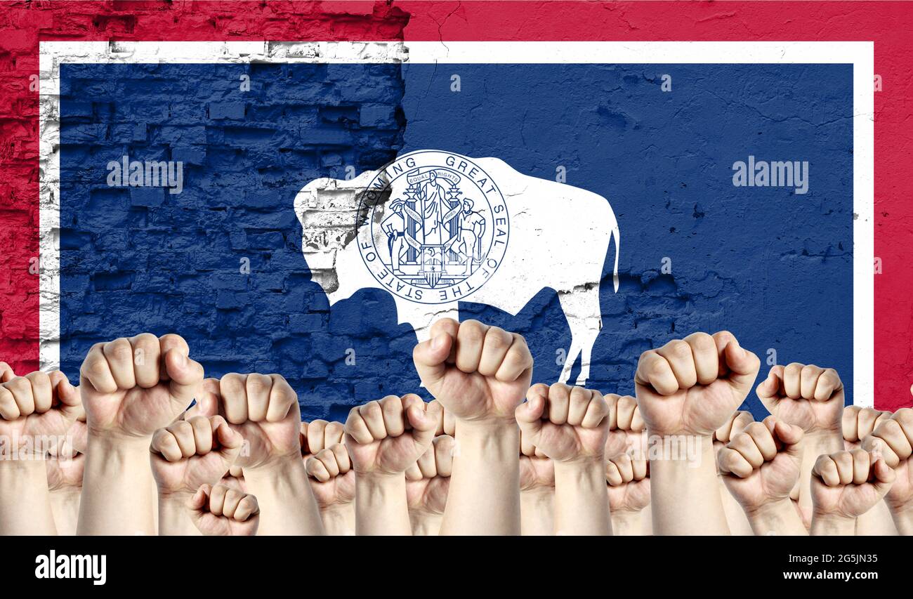 Raised fists of men against the background of the flag of State of Wyoming painted on the wall, the concept of popular unity and the opinion of the ma Stock Photo