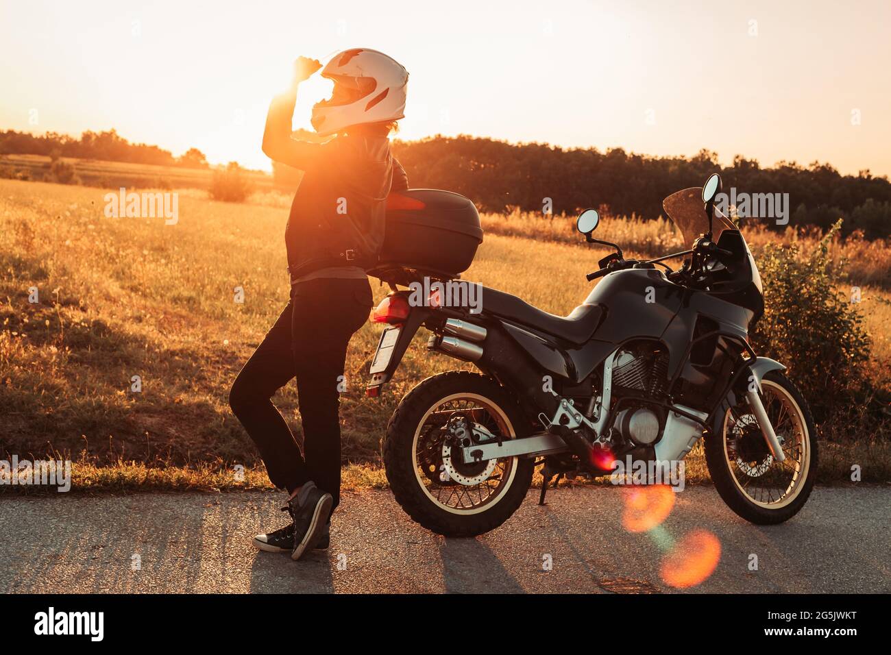 Female biker standing next to her bike, taking a break. Afternoon light, copy space Stock Photo