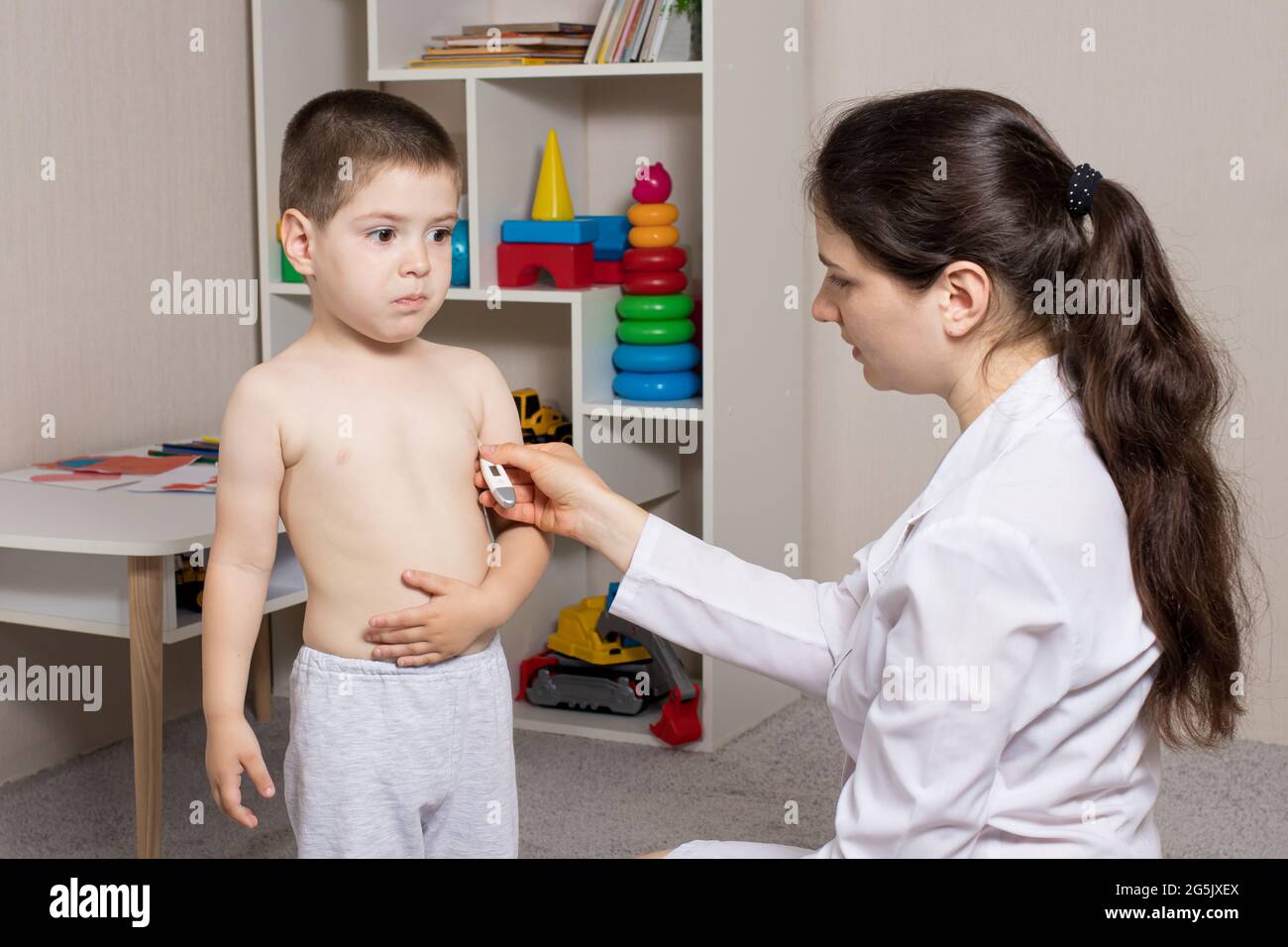 A pediatrician or nurse measures a child body temperature with a thermometer. Fever in children
