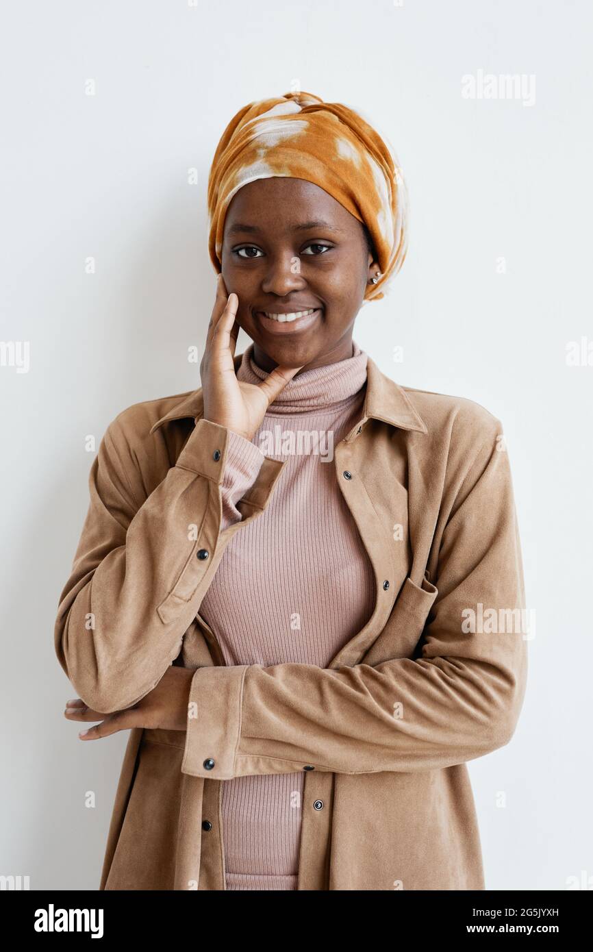 Vertical portrait of smiling African-American woman looking at camera while standing against white wall Stock Photo