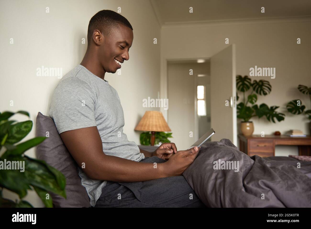 Smiling African man using a tablet and drinking coffee in bed Stock Photo