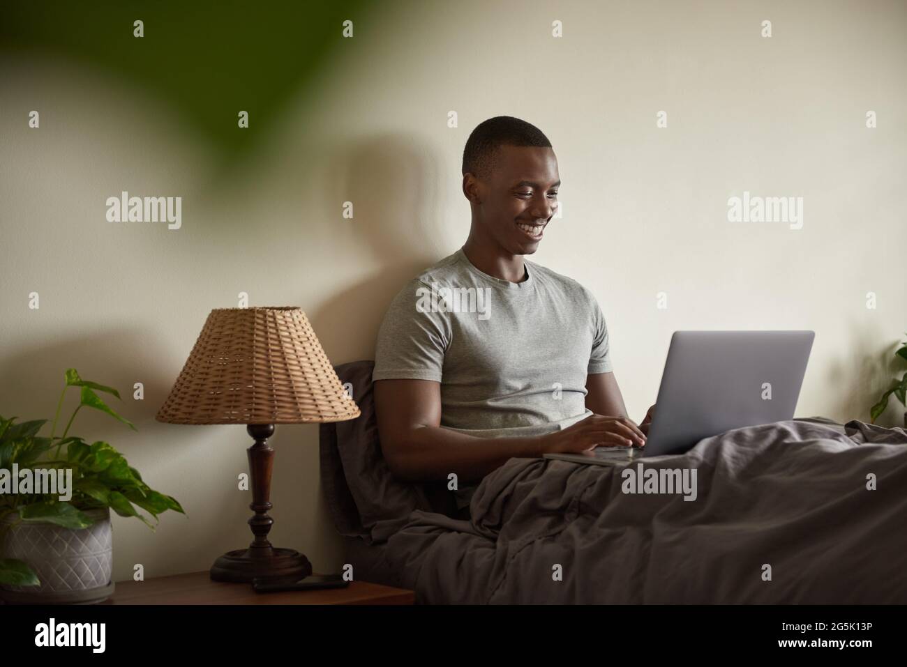 Smiling African man using a laptop in his bed at home Stock Photo