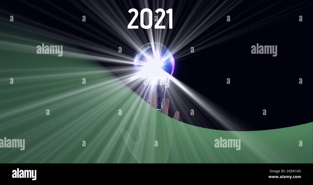 Composition of green copy space over year 2021, hand and lit lightbulb, on black Stock Photo