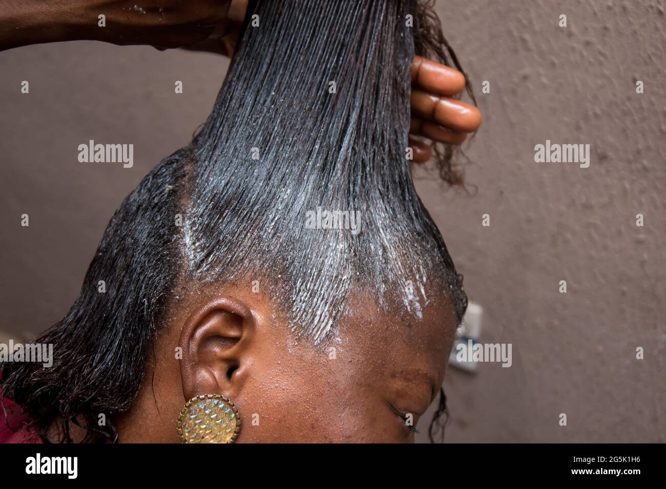 Hairdresser relaxing the hair on an african woman head and also using comb to stretch and apply the relaxer cream through the hair Stock Photo