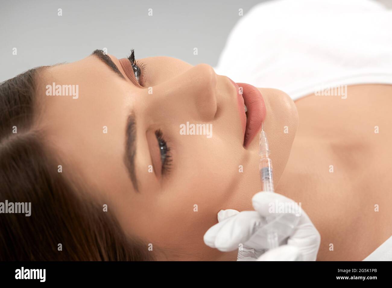 Side view of young attractive woman procedure for lip augmentation in professional salon. Concept of beauty procedure with good mood and with professional cosmetics.  Stock Photo