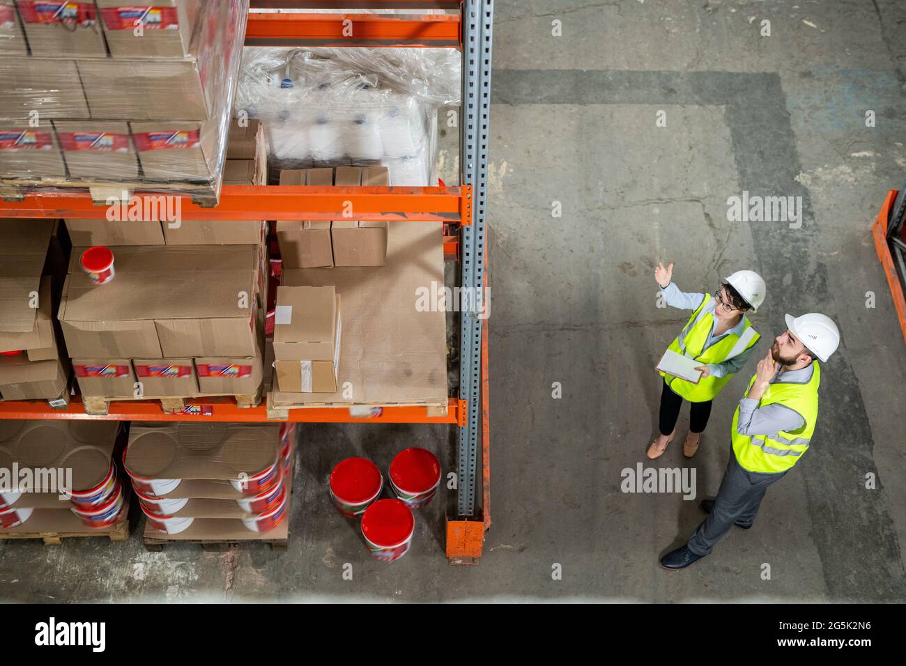 Two workes of warehouse in uniform having discussion in front of rack