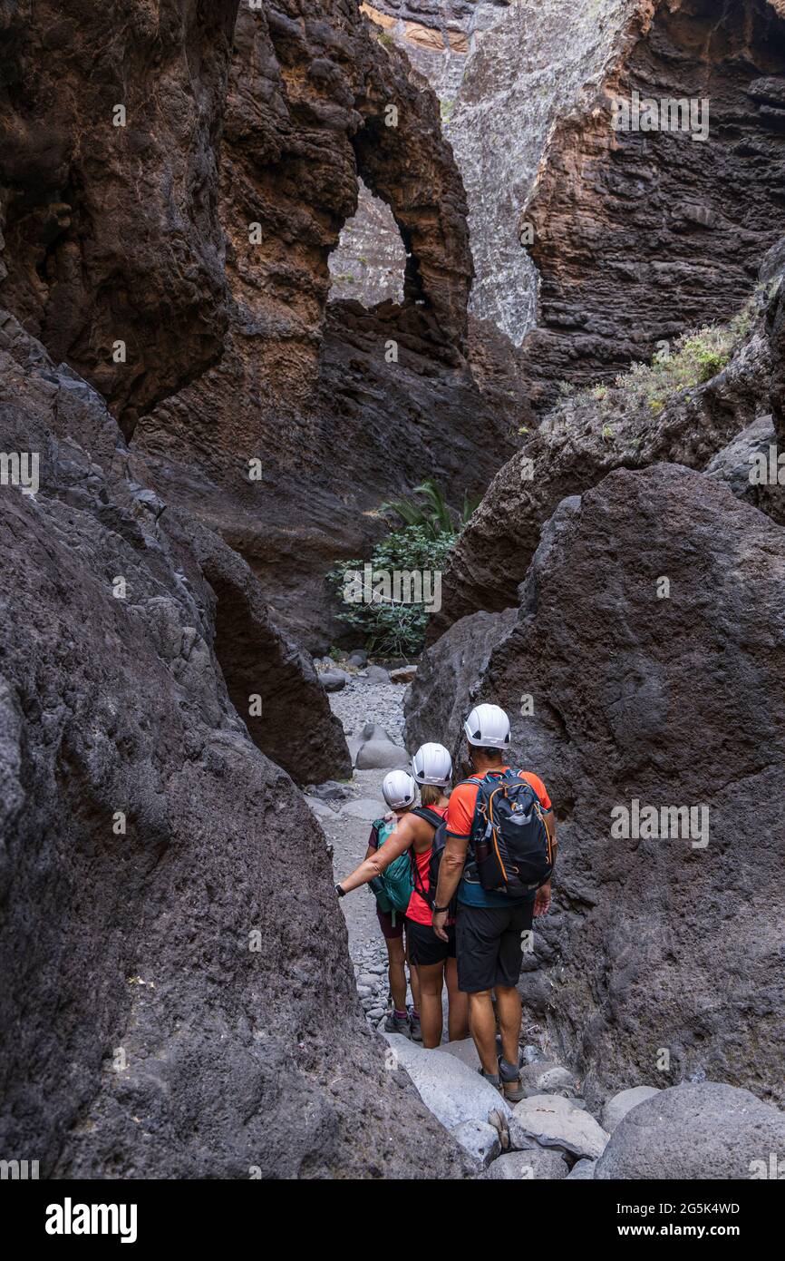 Hikers wearing safety helmets as they walk down the Barranco of Masca, volcanic ravine, gorge, walk down from the mountain village to the coast, Tener Stock Photo