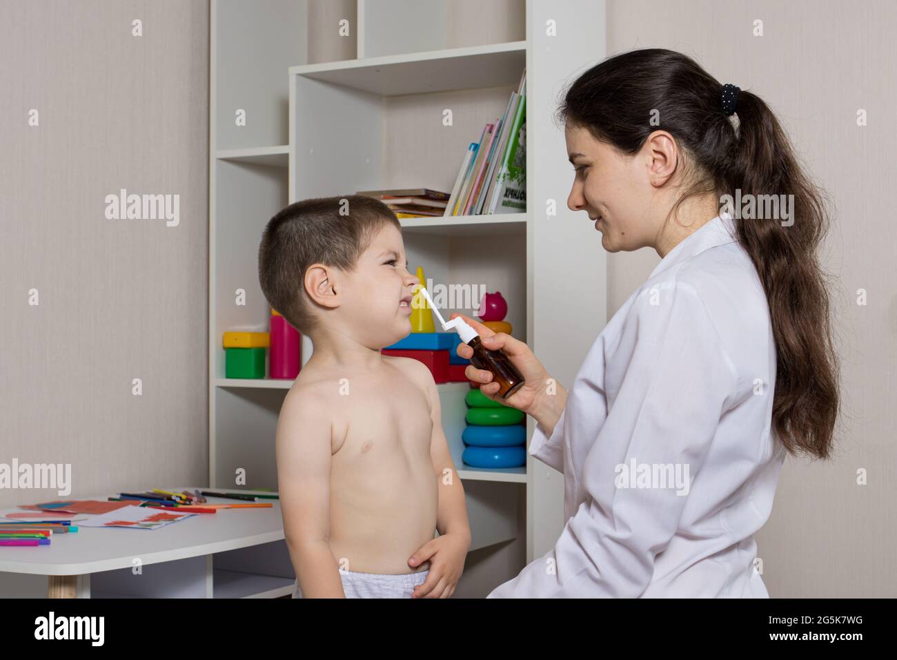 A pediatrician and a boy 3-4 years old. Nasal spray, rhinitis treatment, runny nose. Stock Photo