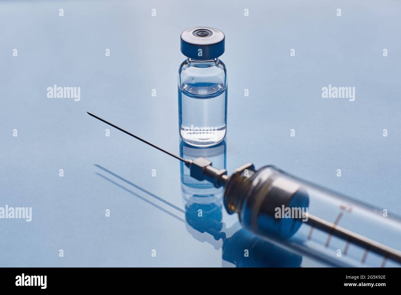 Glass vaccine vial and glass medical syringe on blue glass background ...