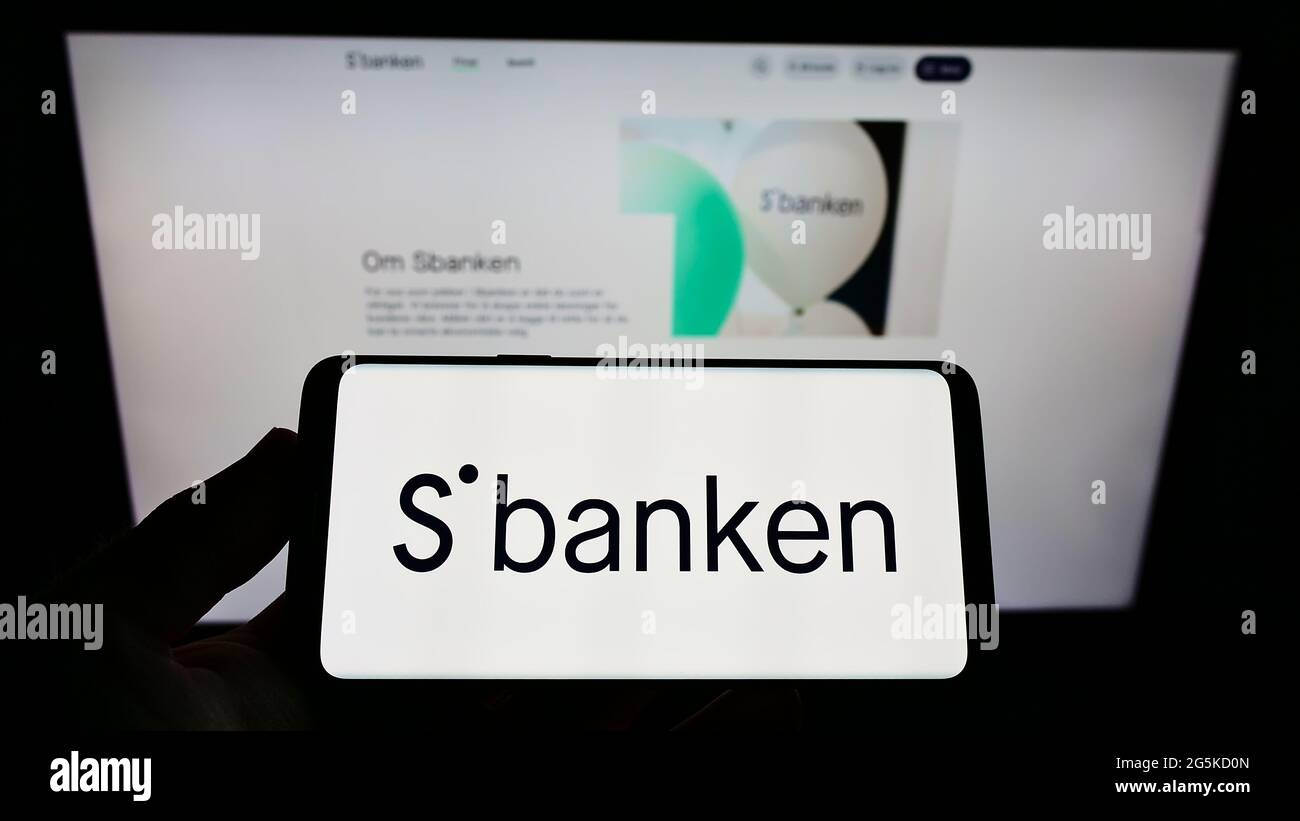 Person holding cellphone with logo of Norwegian online bank Sbanken ASA on screen in front of business webpage. Focus on phone display. Stock Photo