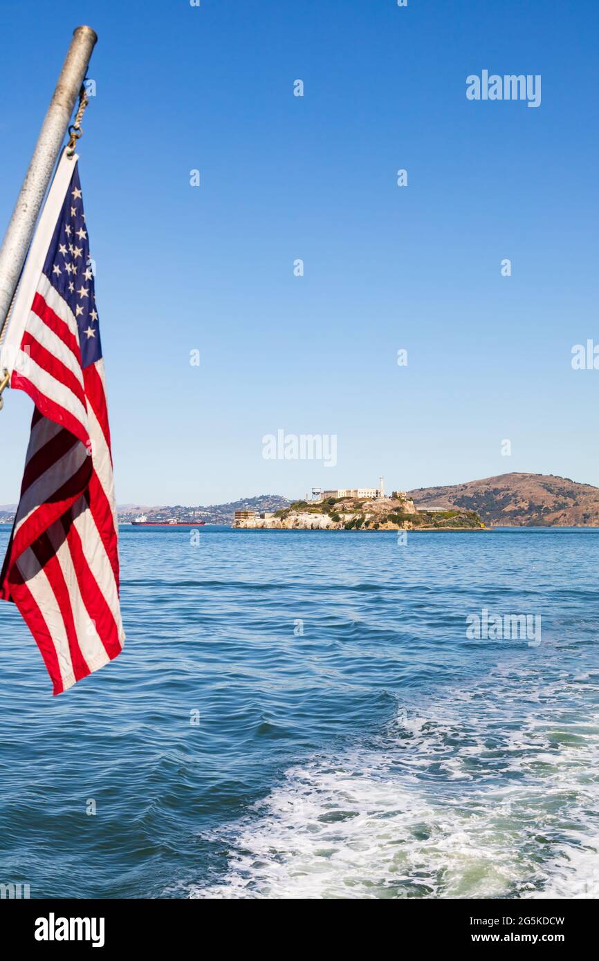 The Stars and Stripes of the United States of America fly from the stern of a boat passing Alcatraz prison island. San Francisco, California, USA Stock Photo