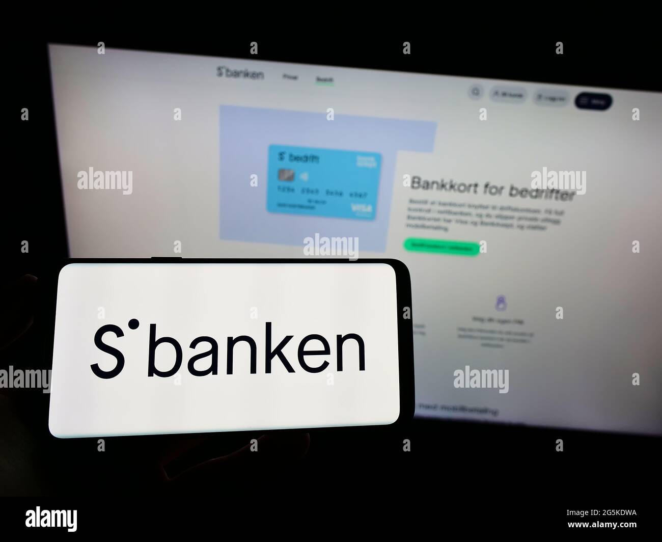 Person holding smartphone with logo of Norwegian online bank Sbanken ASA on screen in front of website. Focus on phone display. Stock Photo