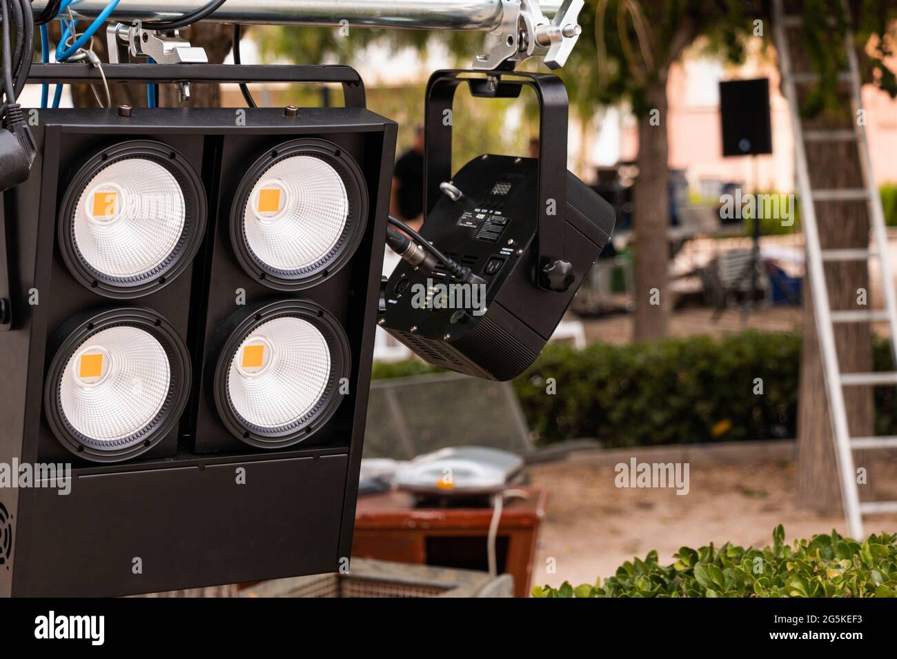 Lighting equipment being set up for a street show. In the foreground are spotlights and in the background, out of focus, electronic equipment, loudspe Stock Photo