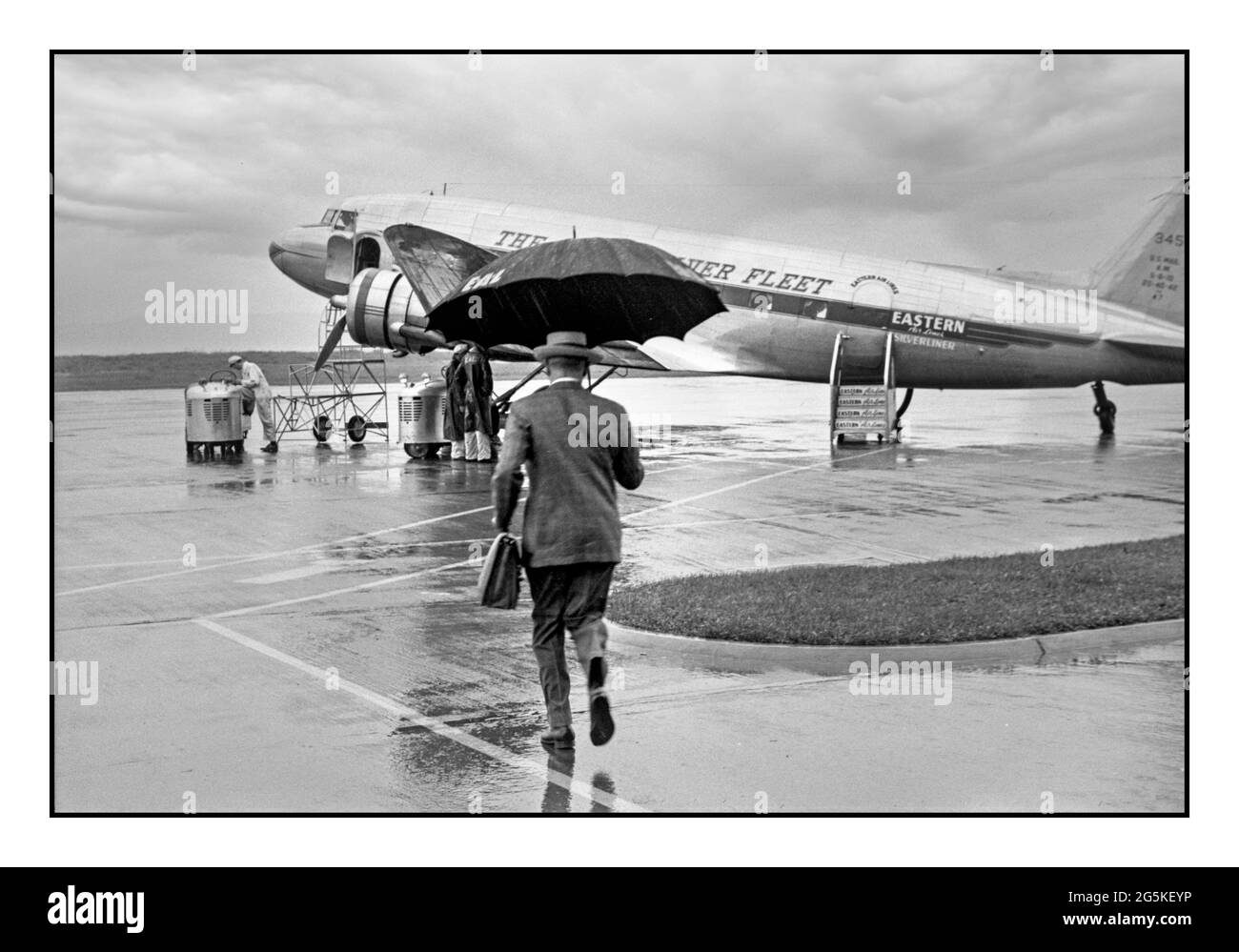 Vintage airline flying business travel 1940's WW2 Golden age of flying  Passenger businessman male man carrying umbrella boarding a DC3 twin propeller Eastern Airline Silver Fleet plane on a rainy day at the municipal airport in Washington, D.C. Jack Delano photographer 1941 July. LOC War Administration World War II United States--District of Columbia--Washington (D.C.) America USA Stock Photo