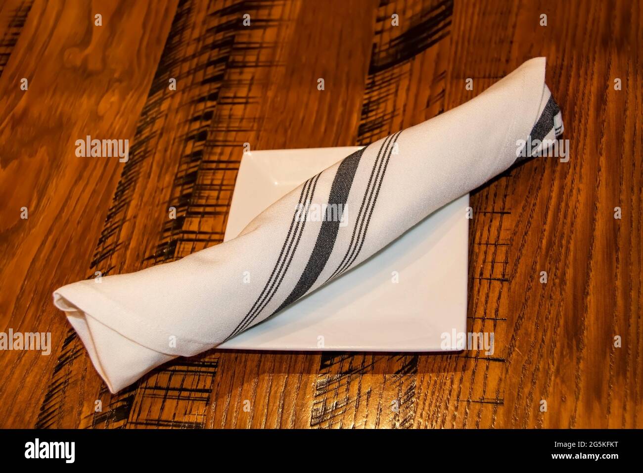 Cuttlery wrapped in a striped linnen napkin lying on a bread dish on a wooden table Stock Photo