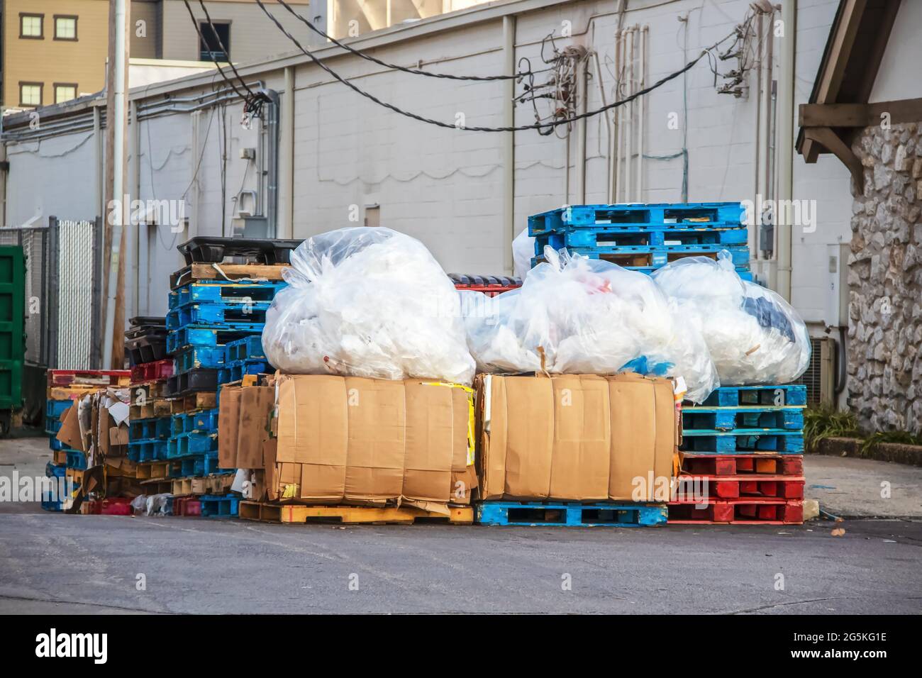 Recyclables in alley between stores in shopping center with bundles of broken down boxes stacks of wooden pallets and huge plastic sacks of plastics a Stock Photo