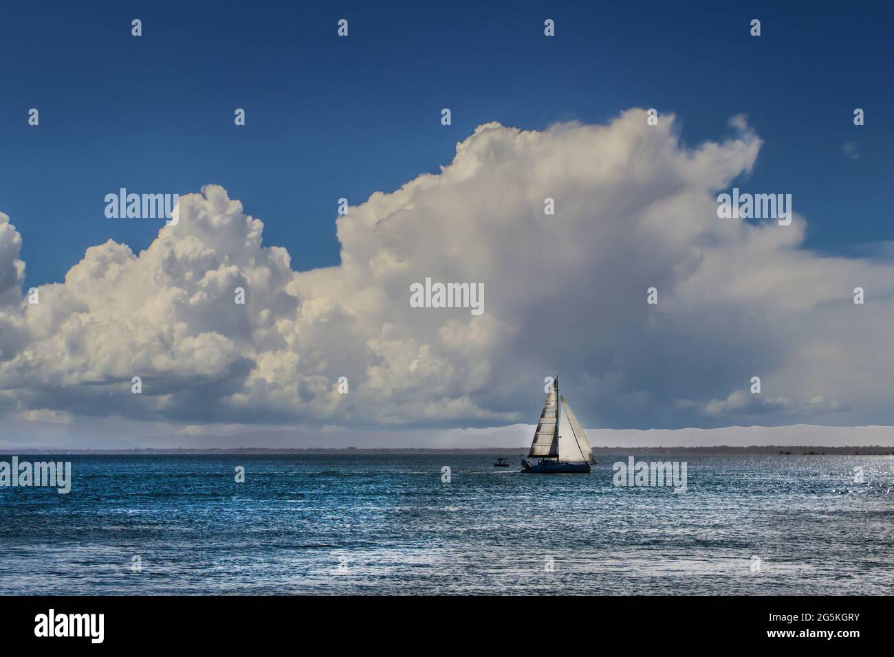 Sailboat out on water with far off coast visiable and huge cloud in blue sky Stock Photo