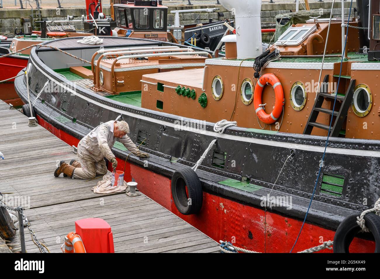 A volunteer from South Eastern Tug Society painting the hull of M.T. Kent tug boat while moored at Chatham Maritime Marina, Kent, England. Stock Photo