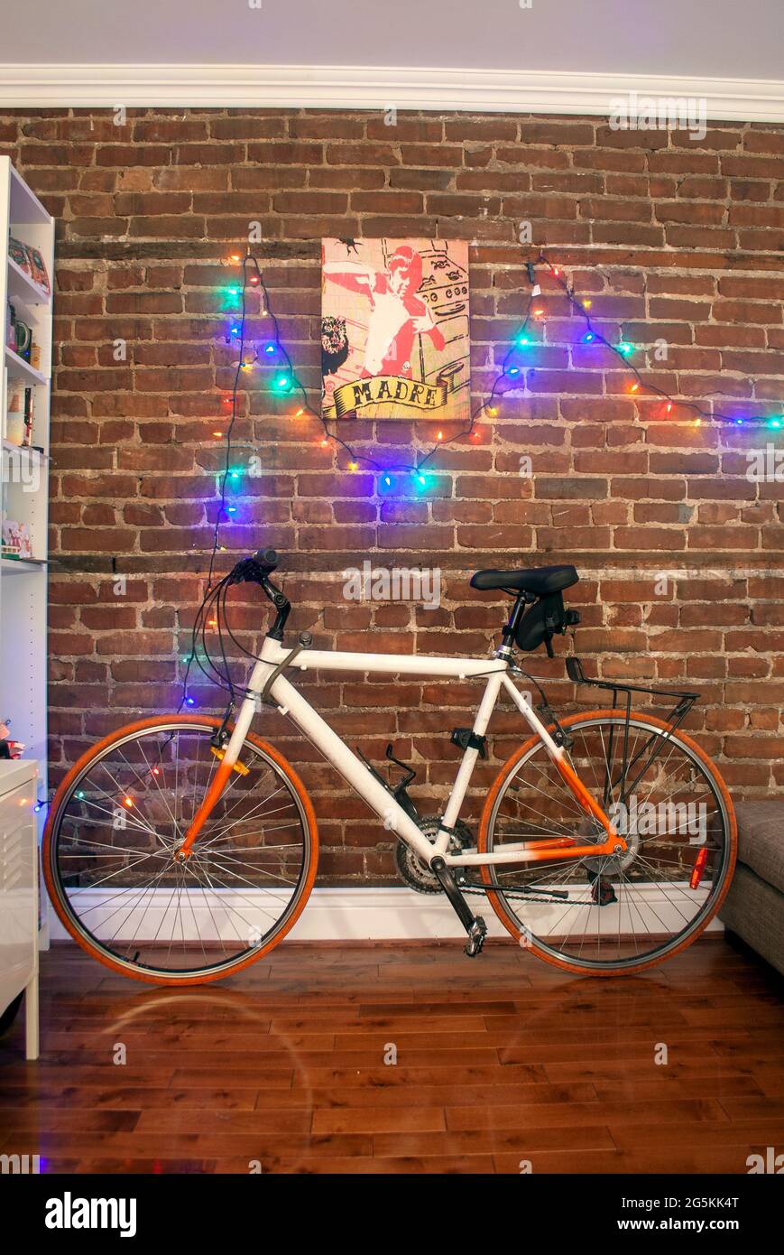 Colorful bicycle leaning against the brick wall of a room with christmas lights strung along the wall Stock Photo