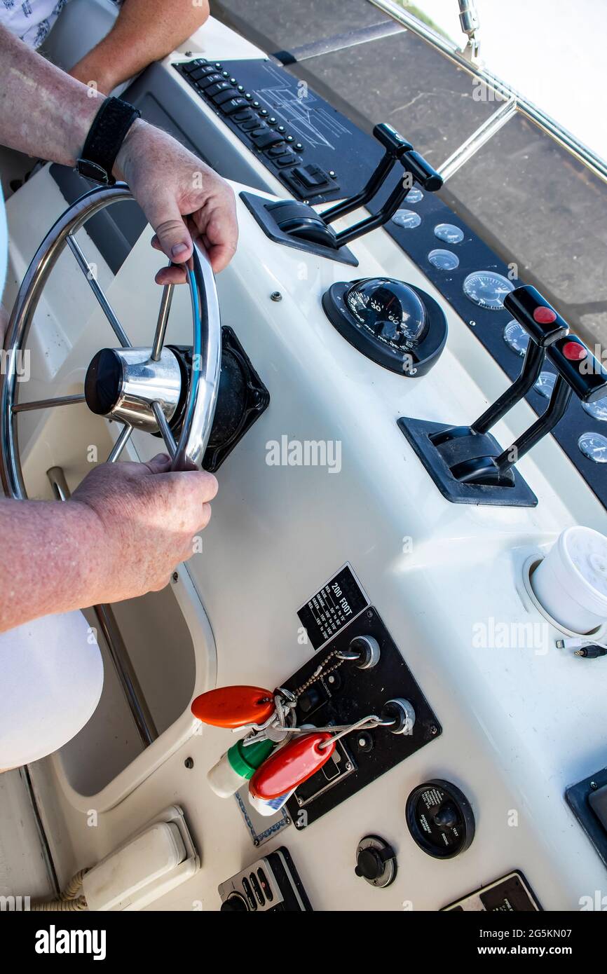 Two men on a boat, with hands and arms showing - one man drives and operates at cockpit and the other is relaxing and watching - unrecognizable Stock Photo