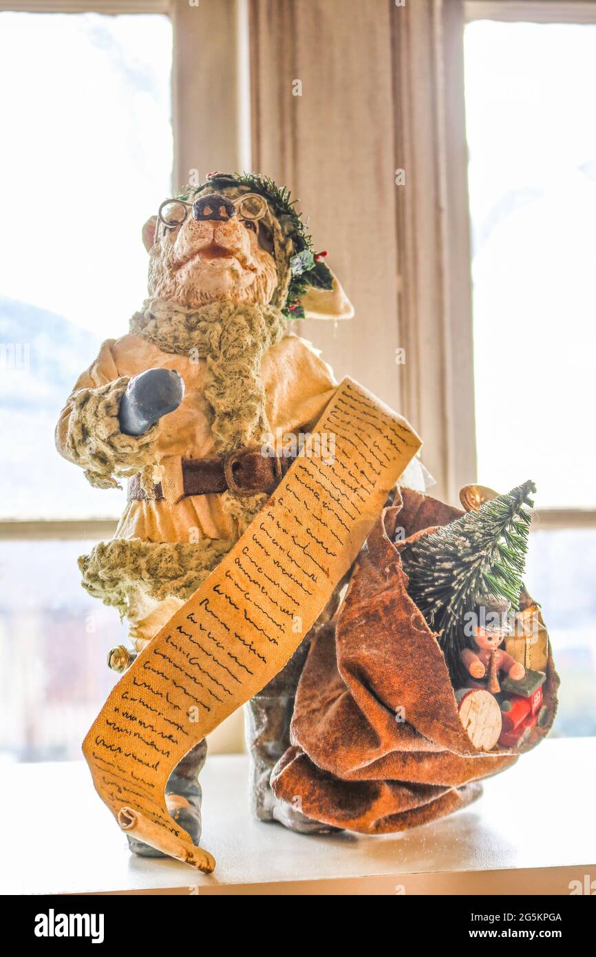 Vintage bear Santa Father Christmas decoration in with bag of toys and long list in front of frosty window with light coming in - Selective focus. Stock Photo
