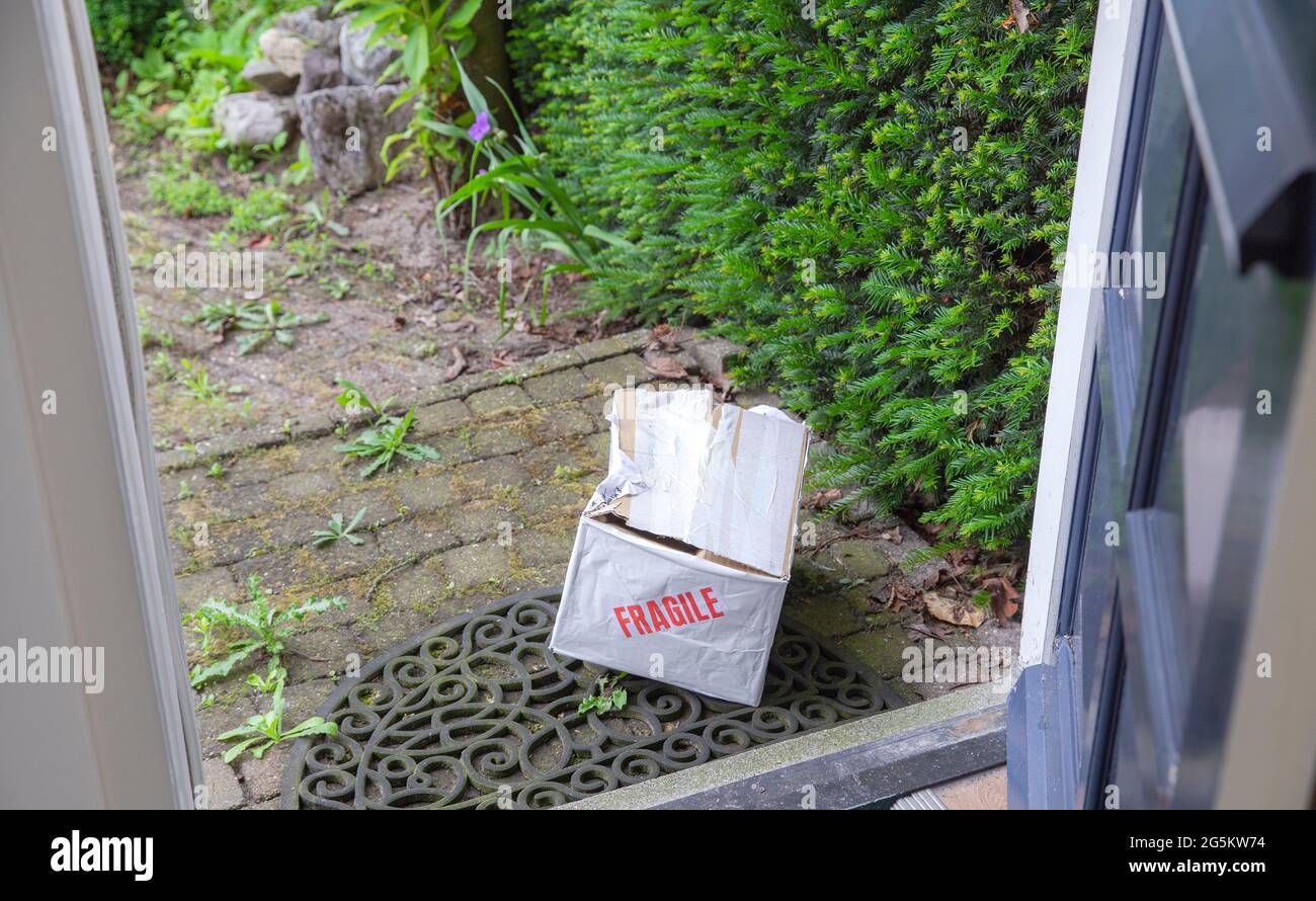 Damaged delivery cardboard box at front door of a house, Fragile