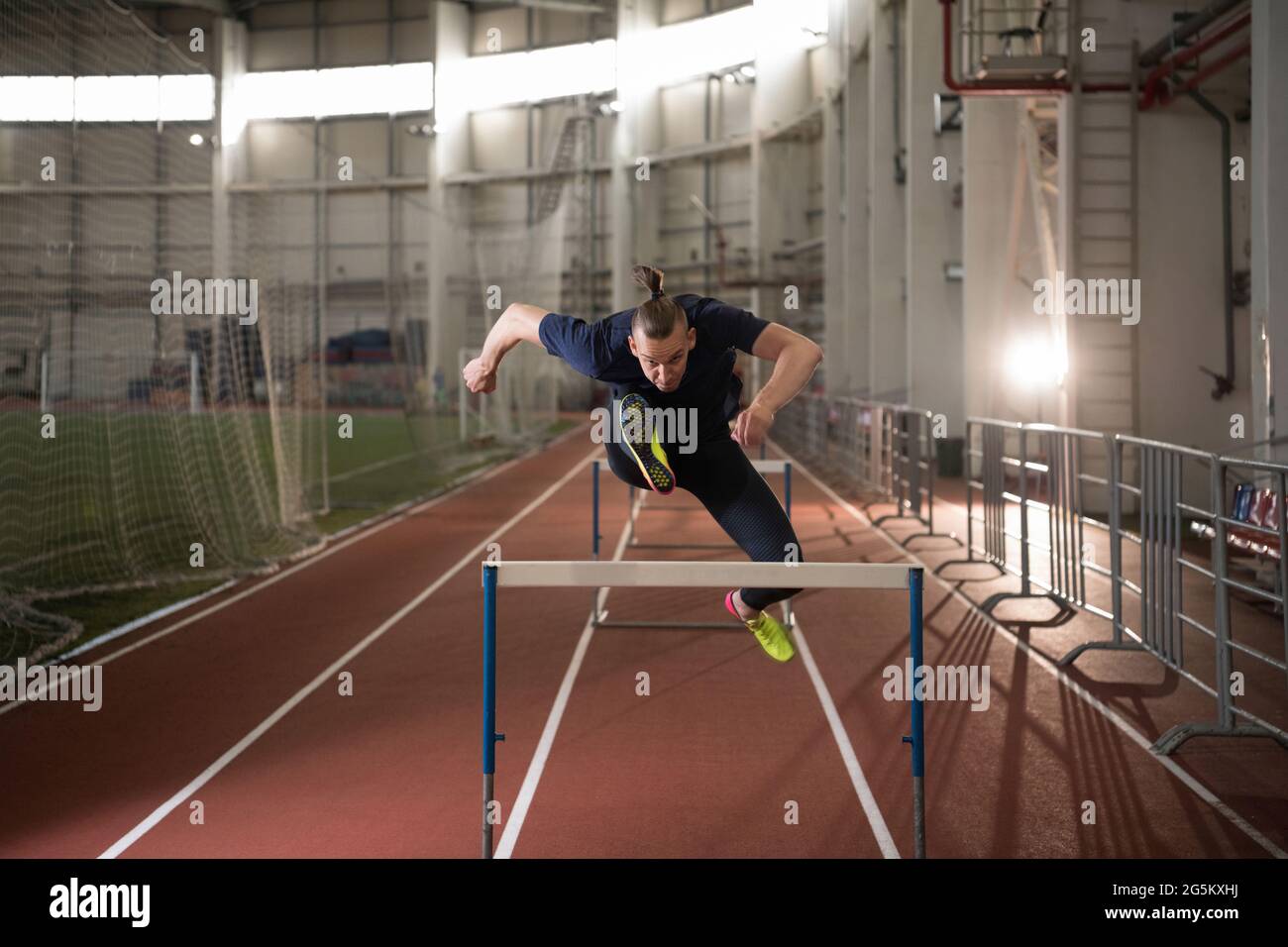 Strong male athlete jumping over hurdle with effort during track and field workout Stock Photo