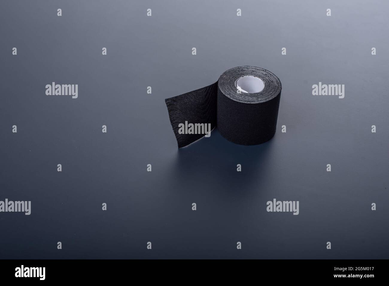 The medical tape lies on a black background. Black roll of kineziotape