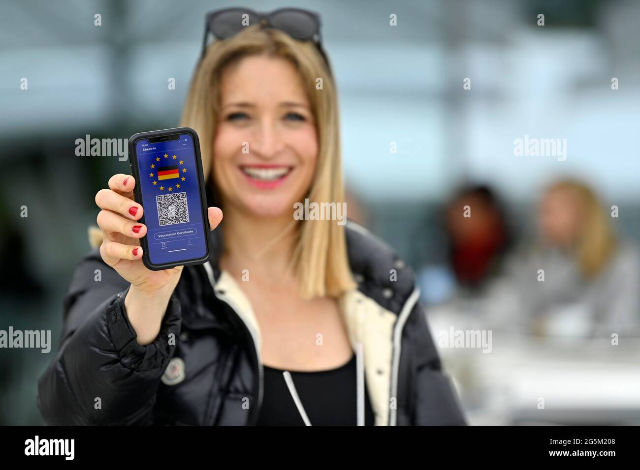 Symbol photo vaccination privilege, smiling woman shows smartphone with digital European vaccination certificate for German citizens, with QR code, Co Stock Photo