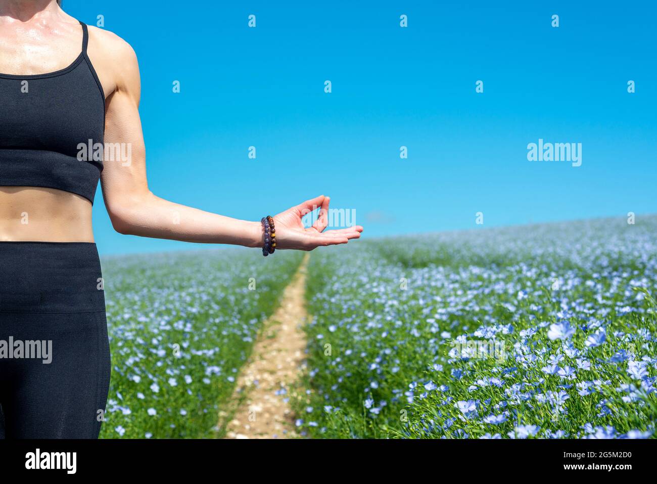 close up of a woman practicing yoga and meditation in a field with wild flowers and blue sky. Stock Photo