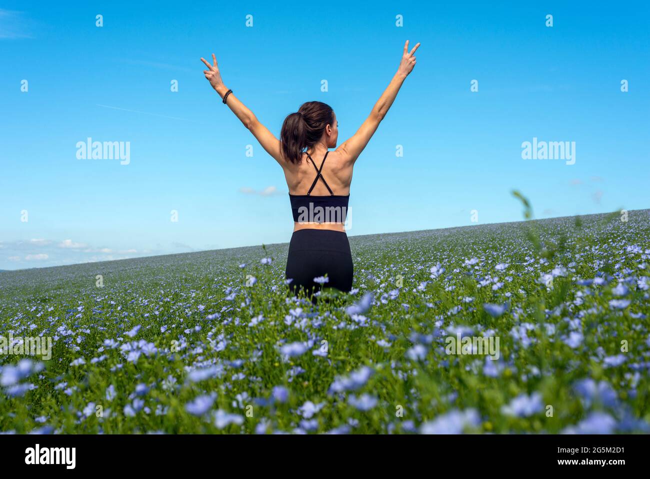 sporty young woman standing in the field of wild flowers with arms stretched out Stock Photo