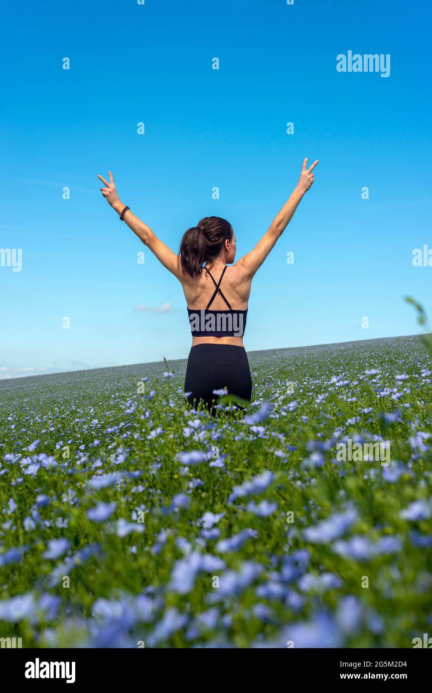 sporty young woman standing in the field of wild flowers with arms stretched out Stock Photo