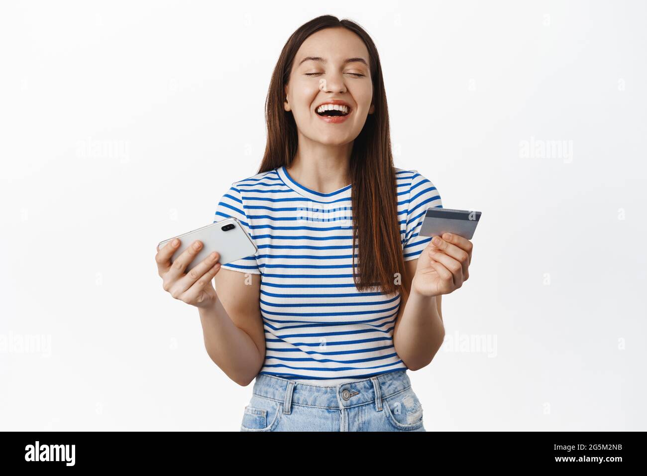Smiling woman looking relieved and satisfied, holding smartphone horizontal and credit card, close eyes from satisfaction, buying app premium Stock Photo