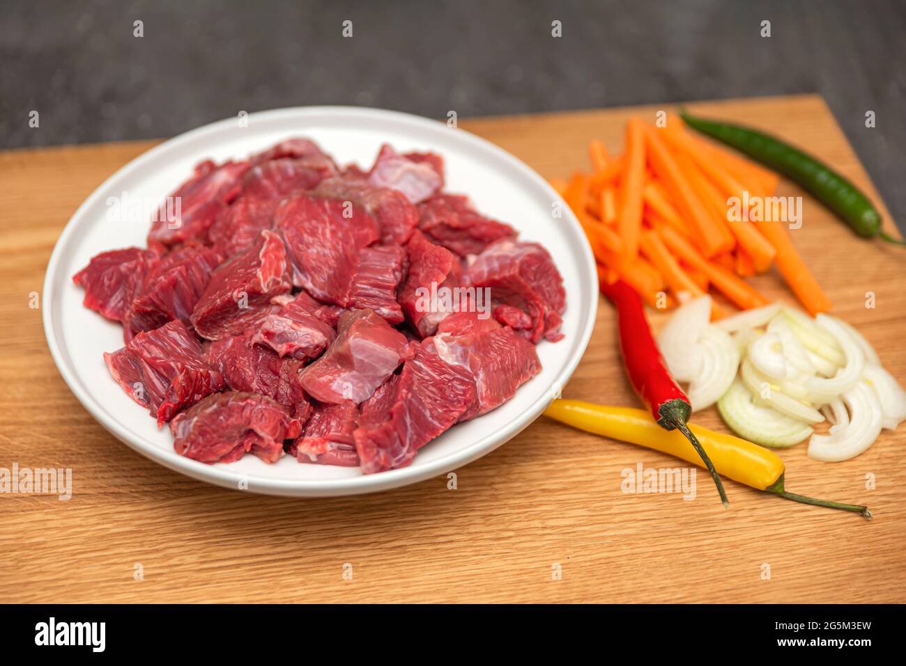 Cooking pilaf in a cauldron, a recipe for real pilaf. Ingredients for cooking pilaf on a wooden background. Onions, peppers, carrots, minced meat lie Stock Photo