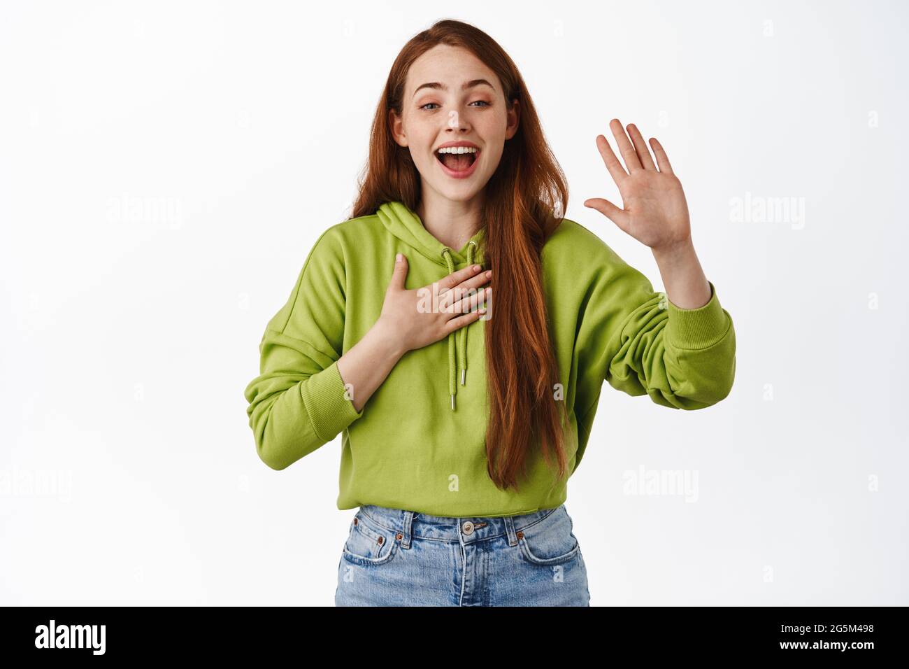 Happy and friendly redhead girl raising hand, put palm on heart and