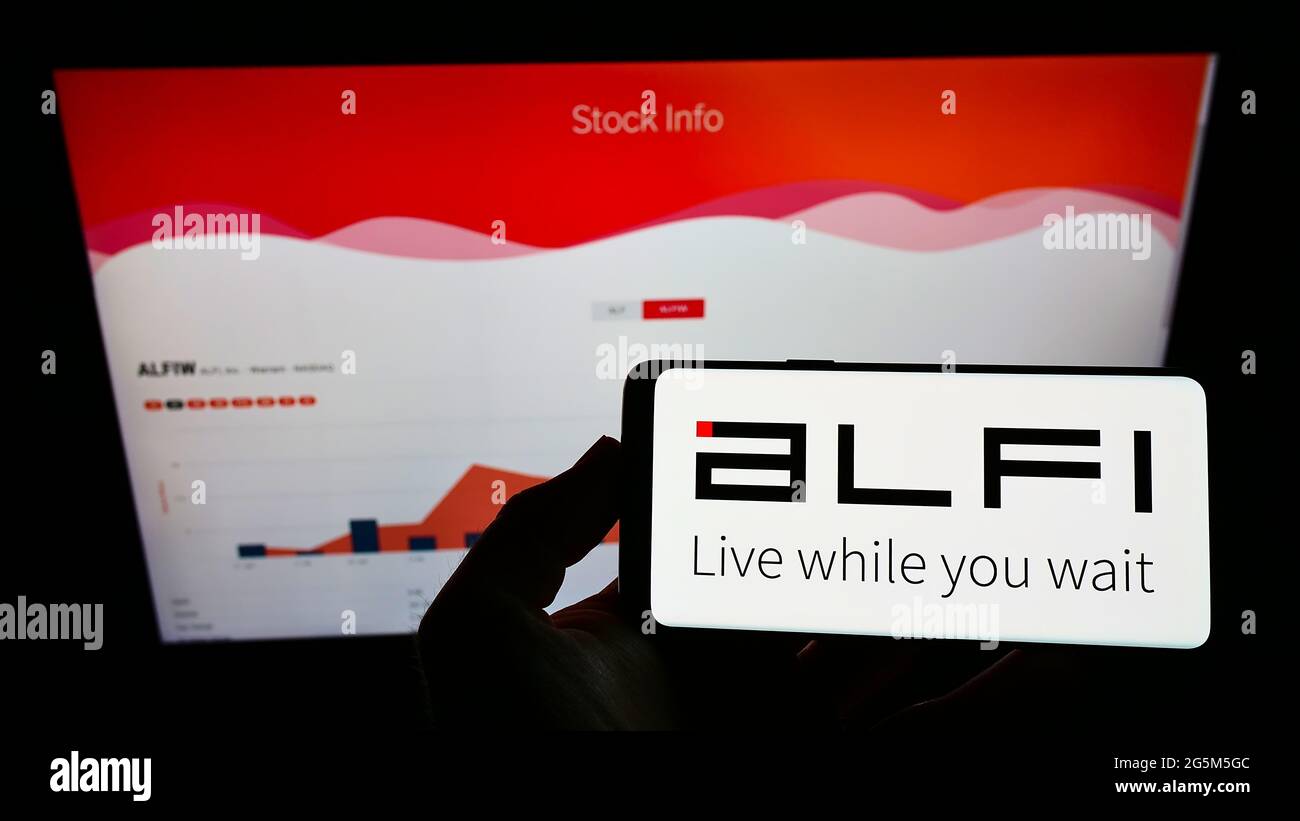 Person holding smartphone with logo of US advertising platform company ALFI Inc. on screen in front of website. Focus on phone display. Stock Photo