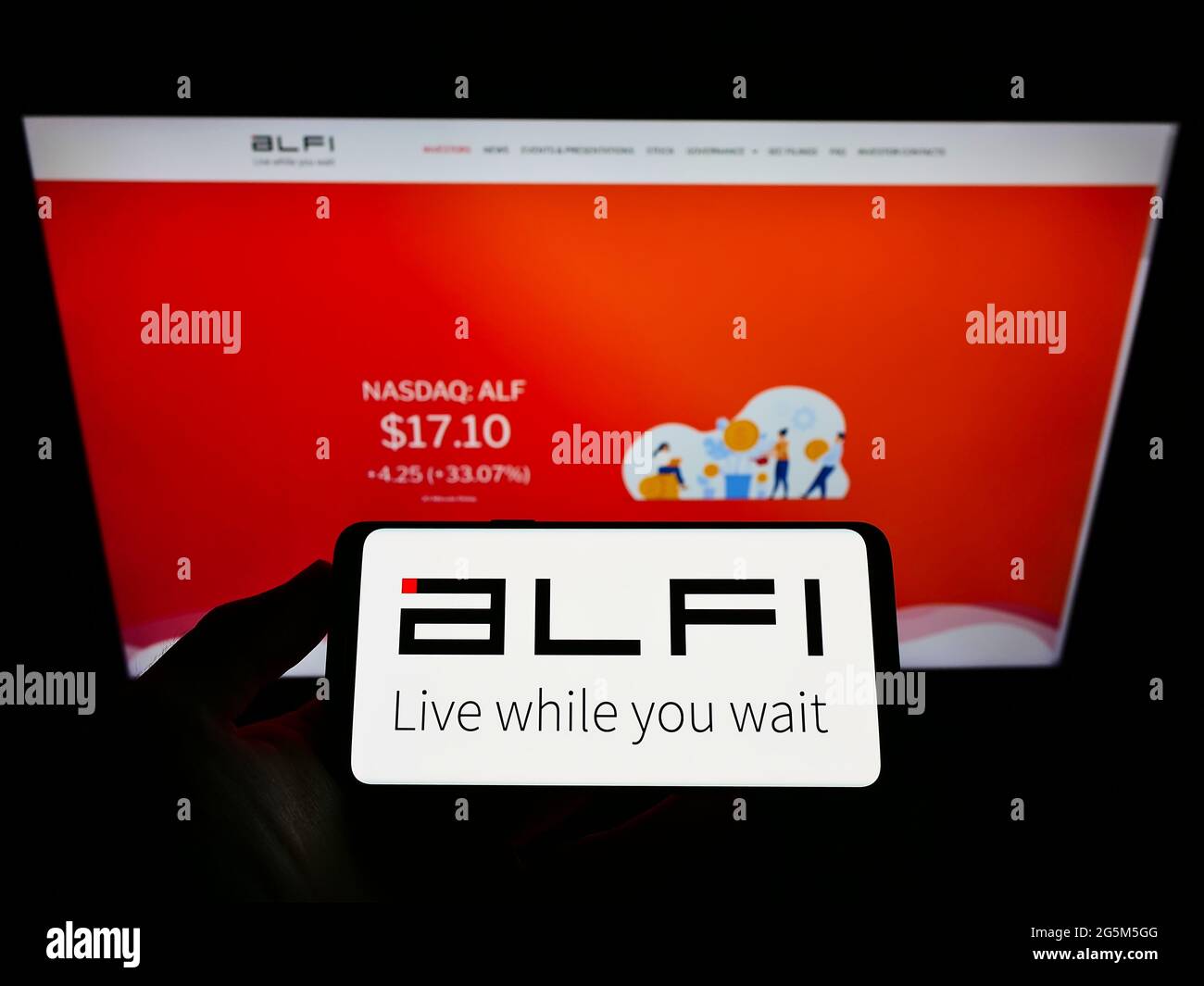 Person holding mobile phone with logo of US advertising platform company ALFI Inc. on screen in front of business web page. Focus on phone display. Stock Photo