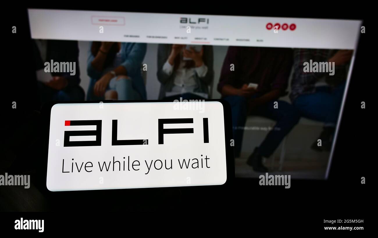 Person holding cellphone with logo of US advertising platform company ALFI Inc. on screen in front of business webpage. Focus on phone display. Stock Photo