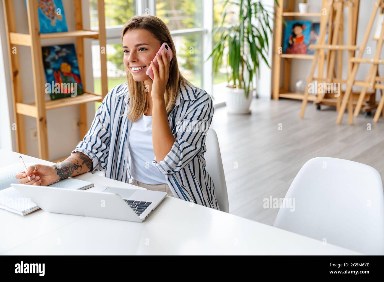 Smiling attractive young woman creative designer using mobile phone while working at the studio Stock Photo