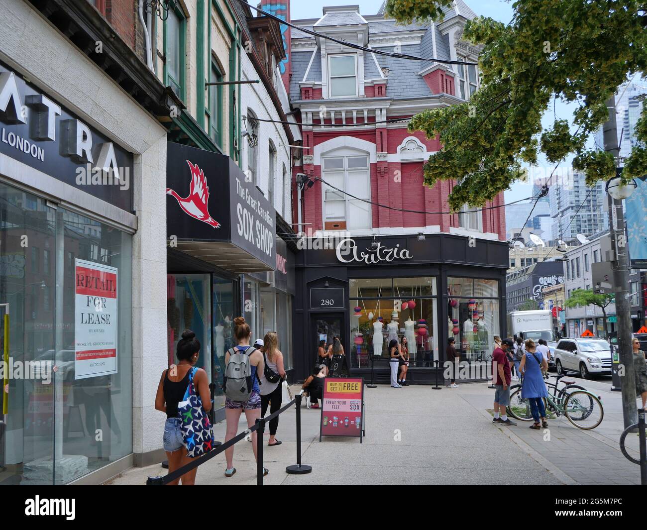 Toronto, Canada - June 28, 2021:  Shoppers line up outside a clothing store on Queen Street West, as the pandemic forces retailers to limit entry. Stock Photo