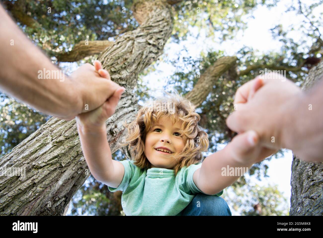 Happy boy climbing a tree during summer time. Fathers hand Stock Photo