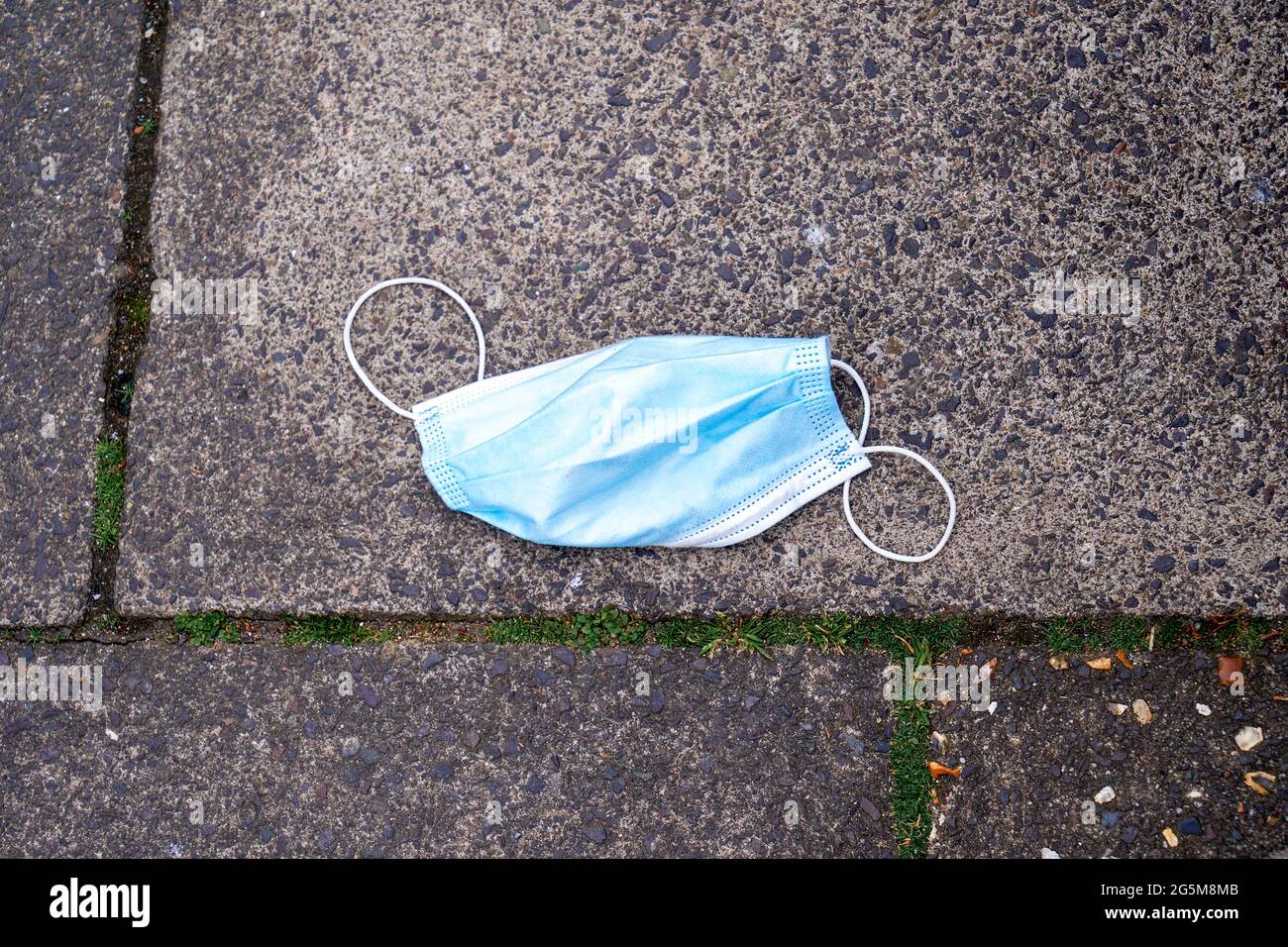 Discarded disposable face mask dropped on pavement Stock Photo
