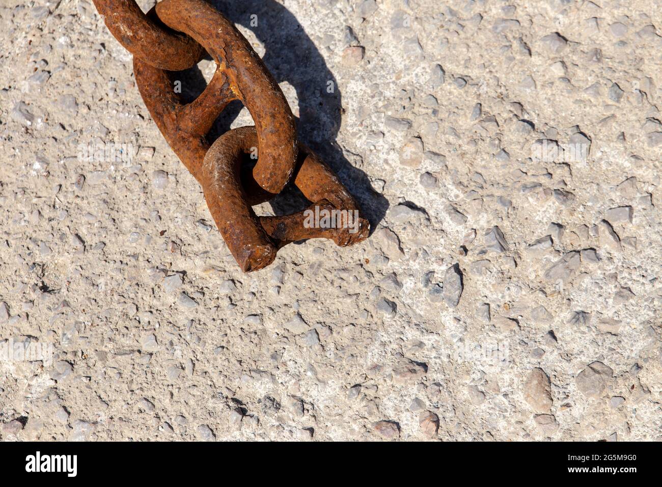 Strong iron mooring chain broken in half, lying on concrete under mid day sun, with copy space. Stock Photo
