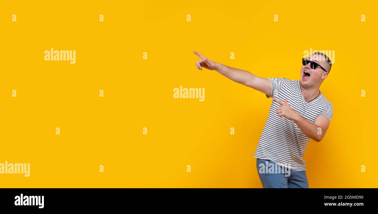 Portrait of funny young man in casual clothes pointing index fingers aside up isolated on yellow orange wall background in studio. People sincere Stock Photo