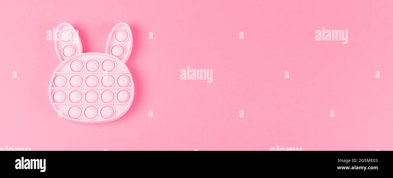 Banner. New silcone toy pop it in shape of bunny on the pink background. New sensory anti-stress toy for children and adult. Copy space. Flat lay. Stock Photo