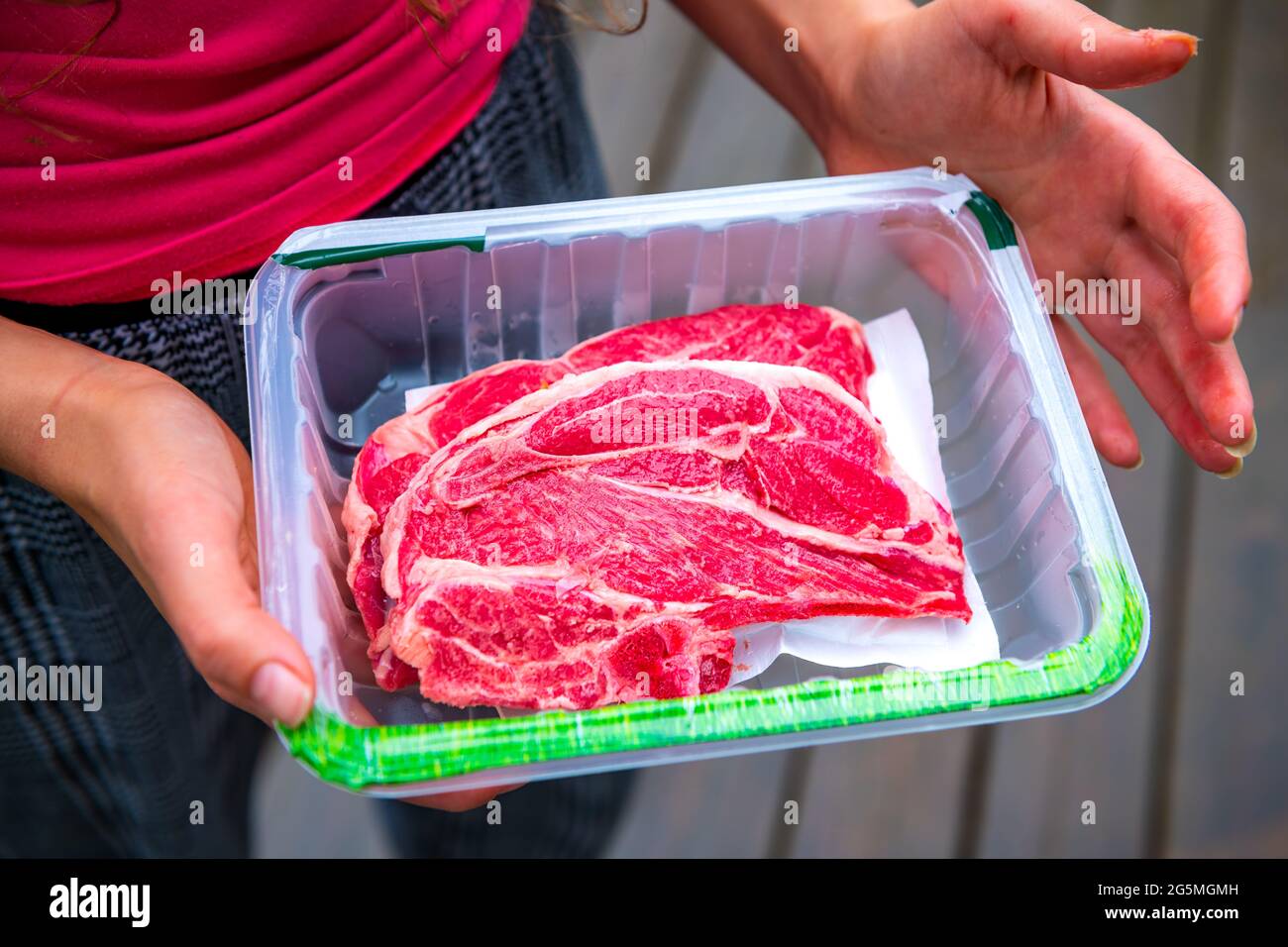 Red raw lamb meat shoulder chops from New Zealand packaged storebought with woman holding open plastic container showing Stock Photo