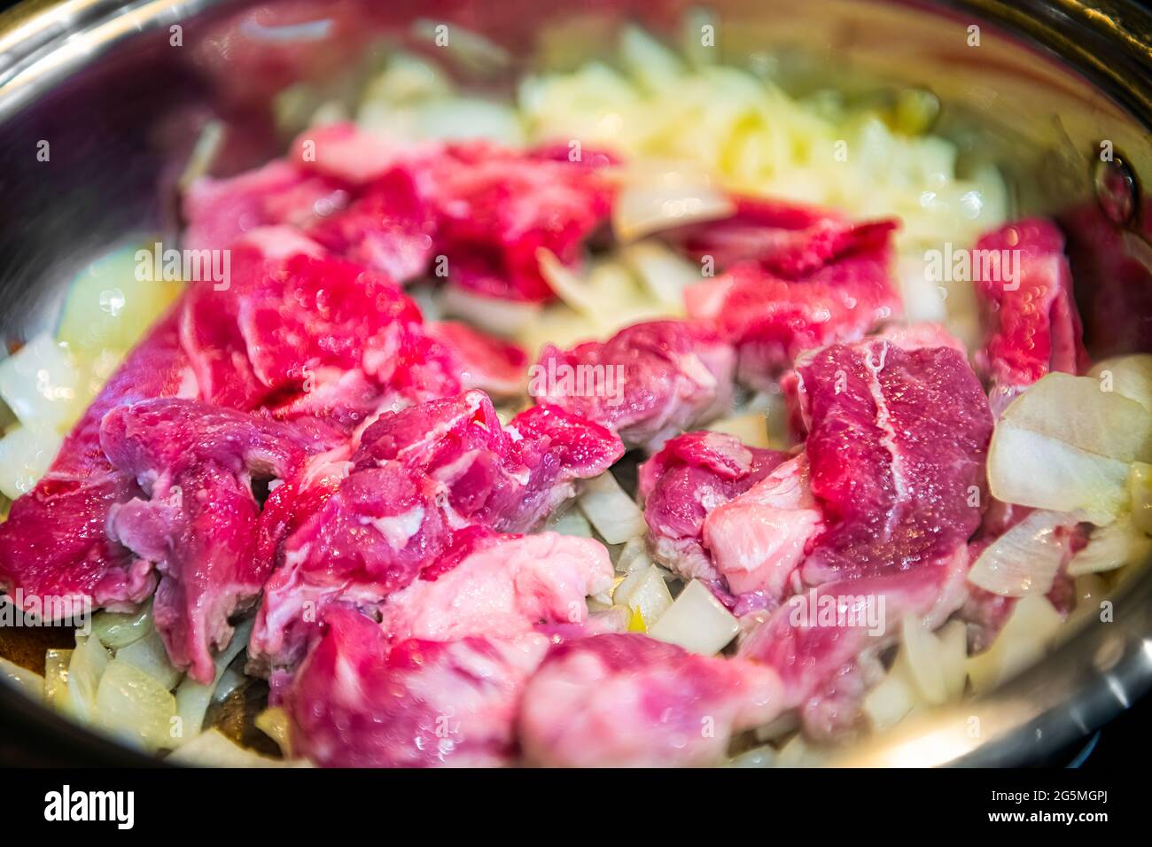 Red raw lamb meat shoulder chops chucks cut in frying pan over onions to make traditional Kazakh or Uzbek pilaf or plov macro closeup Stock Photo