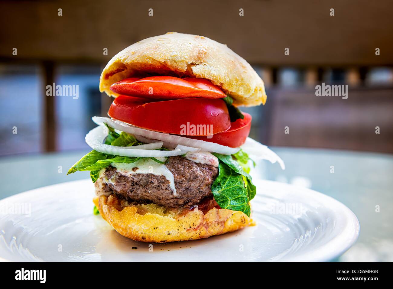 Tall high small burger slider stacked food with melted cheese, patty onions sliced tomatoes and lettuce on bun on white plate macro closeup side view Stock Photo