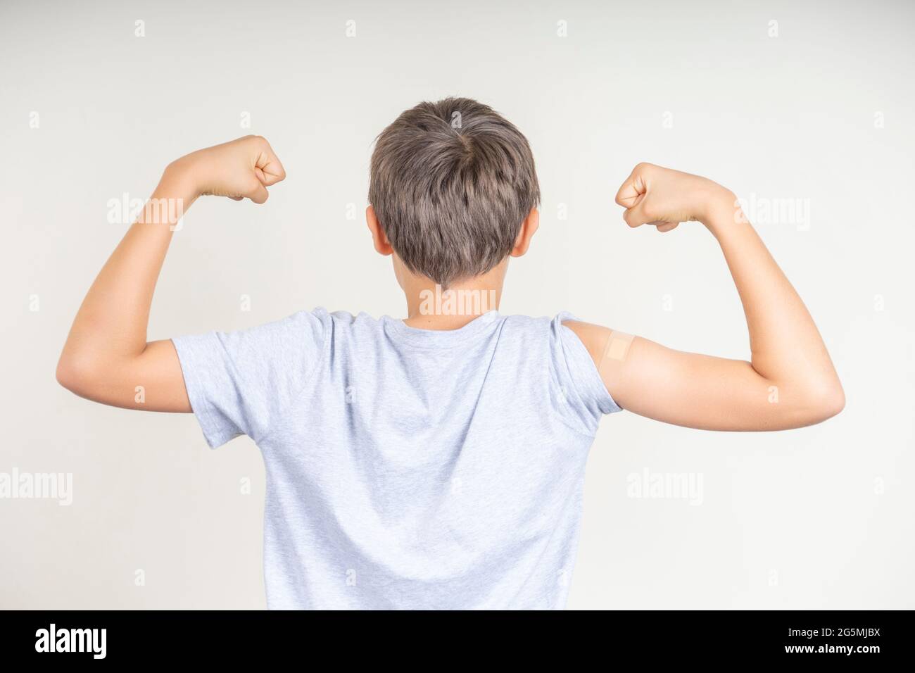 Teenage boy with bandage plaster on his arm makes fist and flexes her bicep after vaccination. Injection covid vaccine, healthcare for children Stock Photo